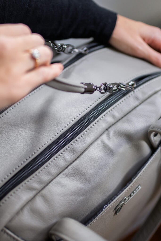 Woman pulls the handle to unzip a Travel Bag from Swagger leather.