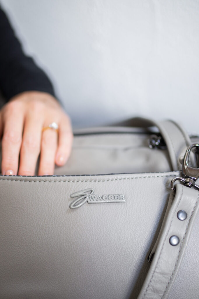 Hand touching a grey Travel Bag from Swagger Leather.